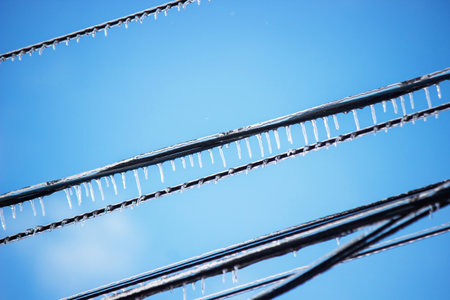 Icy icicles on electric wires against blue sky, freezing rain consequencesの写真素材