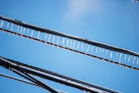 Icy icicles on electric wires against blue sky, freezing rain consequences