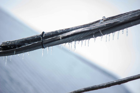 Icy icicles on electric wires against blue sky, freezing rain consequences