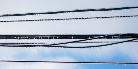 Icy icicles on electric wires against blue sky, freezing rain consequences.の写真素材