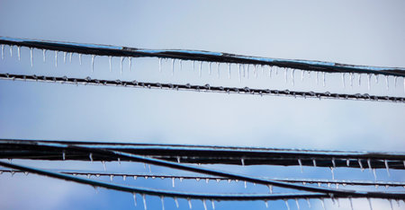 Icy icicles on electric wires against blue sky, freezing rain consequences.の写真素材