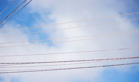 Icy icicles on electric wires against blue sky, freezing rain consequences.