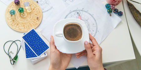 Astrologist workplace: natal charts, tarot cards, and a cup of coffee on table.