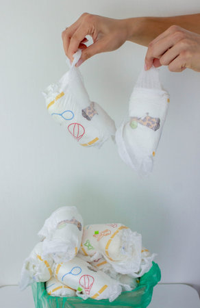 Hand used throwing diaper into trash bin, concept of hygiene and waste disposal.
