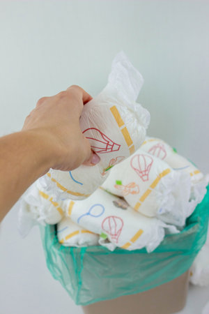 Hand used throwing diaper into trash bin, concept of hygiene and waste disposal.の写真素材
