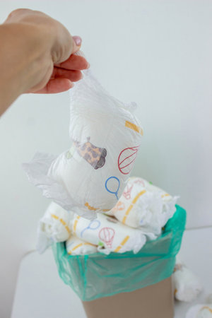 Hand used throwing diaper into trash bin, concept of hygiene and waste disposal.の写真素材