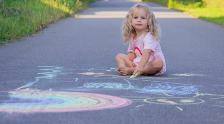 Cute little girl drawing a colorful rainbow with chalk on the asphalt road.の写真素材