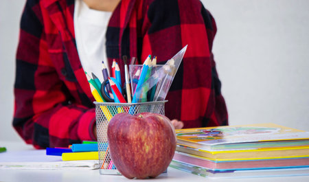 Smiling schoolboy sitting at desk with school supplies on white background.の写真素材