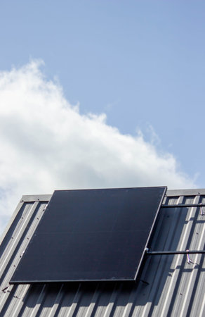 Solar panel installed on a private house metal roof under a blue sky.