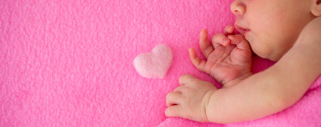 Newborn baby girl sleeping on a pink blanket with a small pink heart - Valentine's Day concept.の写真素材