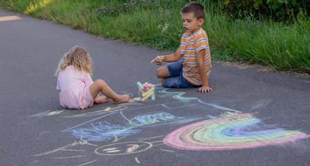 Brother and sister drawing with chalk on a path in the park on a sunny summer day.の写真素材