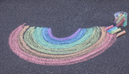 Colorful rainbow drawn with chalk on asphalt pavement with a bucket of crayons.