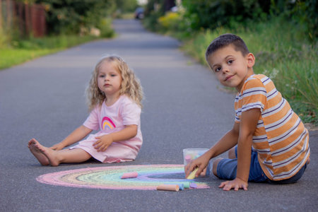 Two happy children drawing colorful rainbow with chalk on asphalt on a summer day.の写真素材