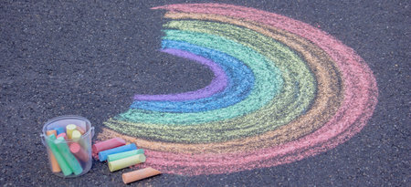 Colorful rainbow drawn with chalk on asphalt pavement with a bucket of crayons.