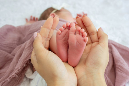 Mother's hands holding tiny newborn baby feet on pink textile background, closeup