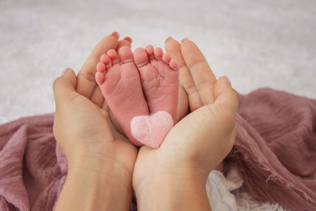Mother's hands holding tiny newborn baby feet on pink textile background, closeup