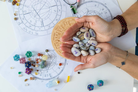 Astrologist hands holding numerology stones over natal charts and zodiac wheel.の写真素材
