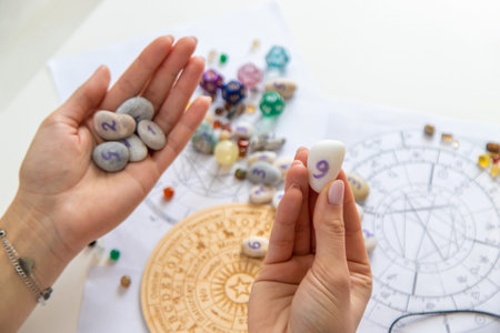 Astrologist hands holding numerology stones over natal charts and zodiac wheel.の写真素材