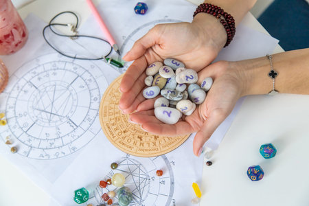 Astrologist hands holding numerology stones over natal charts and zodiac wheel.の写真素材