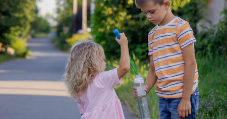 Brother and sister playing with soap bubbles on a country road in summer