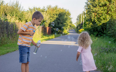 Older brother blowing soap bubbles for his little sister on a country road.の写真素材