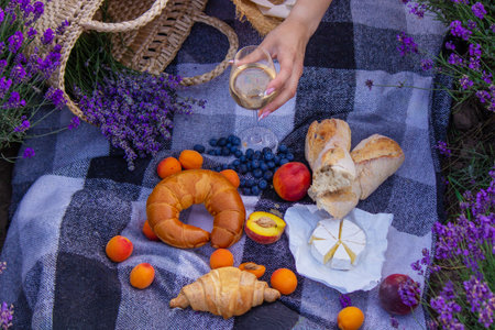 Aesthetic picnic in lavender: wine, fruits, cheese and croissants on a blanket