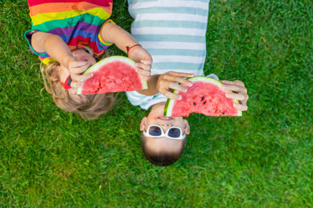 Happy children in sunglasses eating watermelon slices on green grass.の写真素材