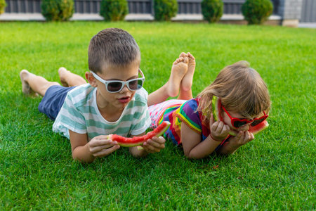 Happy children in sunglasses eating watermelon slices on green grass.の写真素材