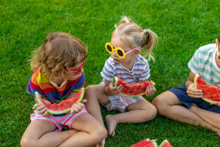 Happy children in sunglasses eating watermelon slices on green grass.の写真素材
