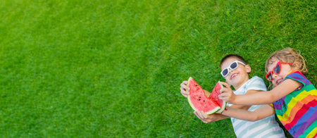 Happy children in sunglasses eating watermelon slices on green grass.の写真素材