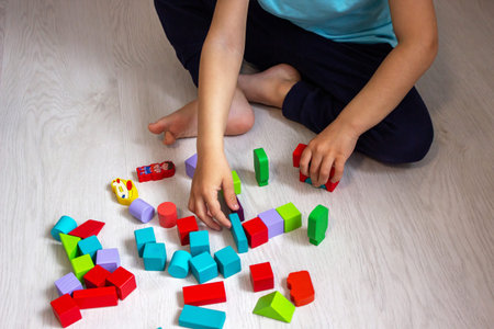 Child playing with colorful wooden blocks on the floor, top view