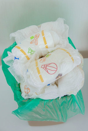 Overfilled trash can with dirty baby diapers and open lid.