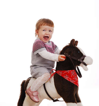 Little girl learning to balance on her first toy horse isolated on a whiteの写真素材