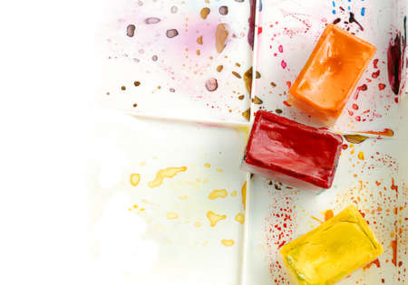 Tree bright watercolor cases on a paint box with colorful splashes in front of white backgroundの写真素材