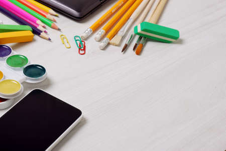 School and student supplies with closed slim notebook and smartphone on a white wooden table surfaceの写真素材
