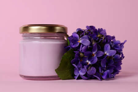 Organic cosmetic cream with beautiful violet flowers on pink backgroundの写真素材