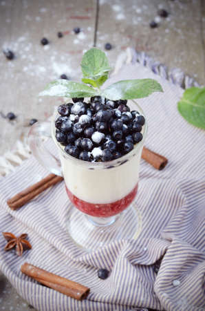 Delicious parfait dessert with bilberry, milk souffle and jello layers. Frozen treat in a glass on rustic wooden backgroundの写真素材