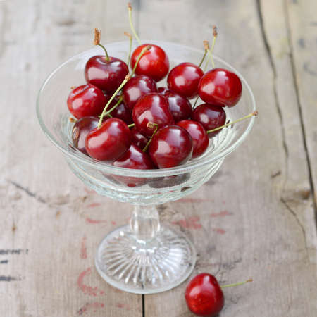 Fresh ripe red cherries berries in vintage crystal vase on old rustic wooden tableの写真素材