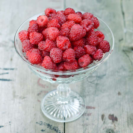 Fresh ripe raspberries in vintage crystal vase on old rustic wooden tableの写真素材