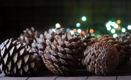 Christmas card with fir cones and beautiful bokeh lights from garland on wooden background, country...