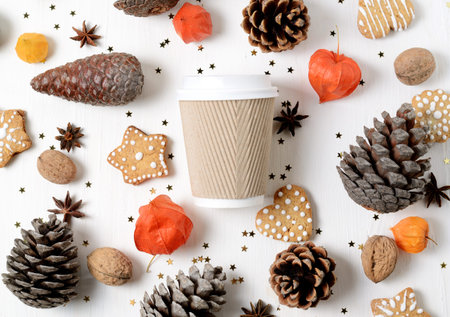 Takeaway paper coffee cup among cookies, pine cones and other christmas decor. Top view trendy photo...