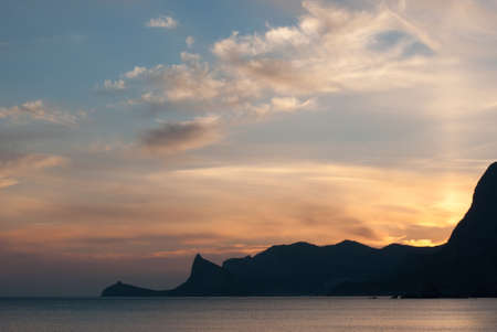Beautiful bright sunset on the Black Sea in the Sudak. Seaside with outline of cape Kapchik. Crimea landscape.の写真素材