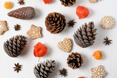 Bright top view Christmas layout with gingerbread cookies, pine cones and orange physalis on a white...
