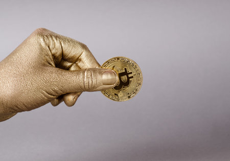 Golden hand holds physical coin of cryptocurrency bitcoin.