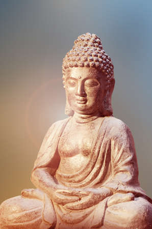 Buddha statue sitting in meditation pose against blurred golden background.の写真素材