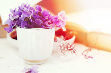 Still life with violet in white cup, old books and date fruits in a plate. Romantic floral...