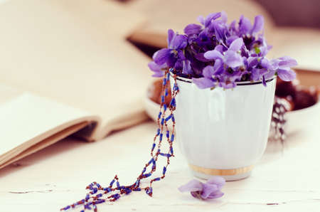 Still life with violet in white cup, old books. Romantic spring floral background.の写真素材