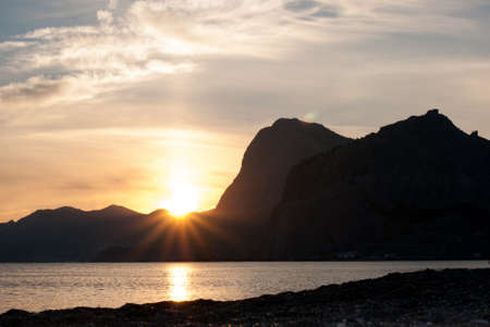 Beautiful bright sunset on the Black Sea in the Sudak. Seaside with outline of cape Kapchik. Crimea landscape.の写真素材