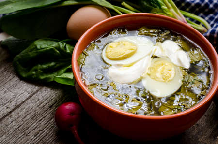Green borscht with sorrel, spinach and potato, topped with boiled egg and sour cream on a vintage wooden table.の写真素材