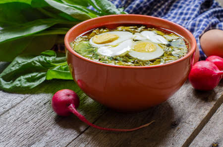 Green borscht with sorrel, spinach and potato, topped with boiled egg and sour cream on a vintage wooden table.の写真素材